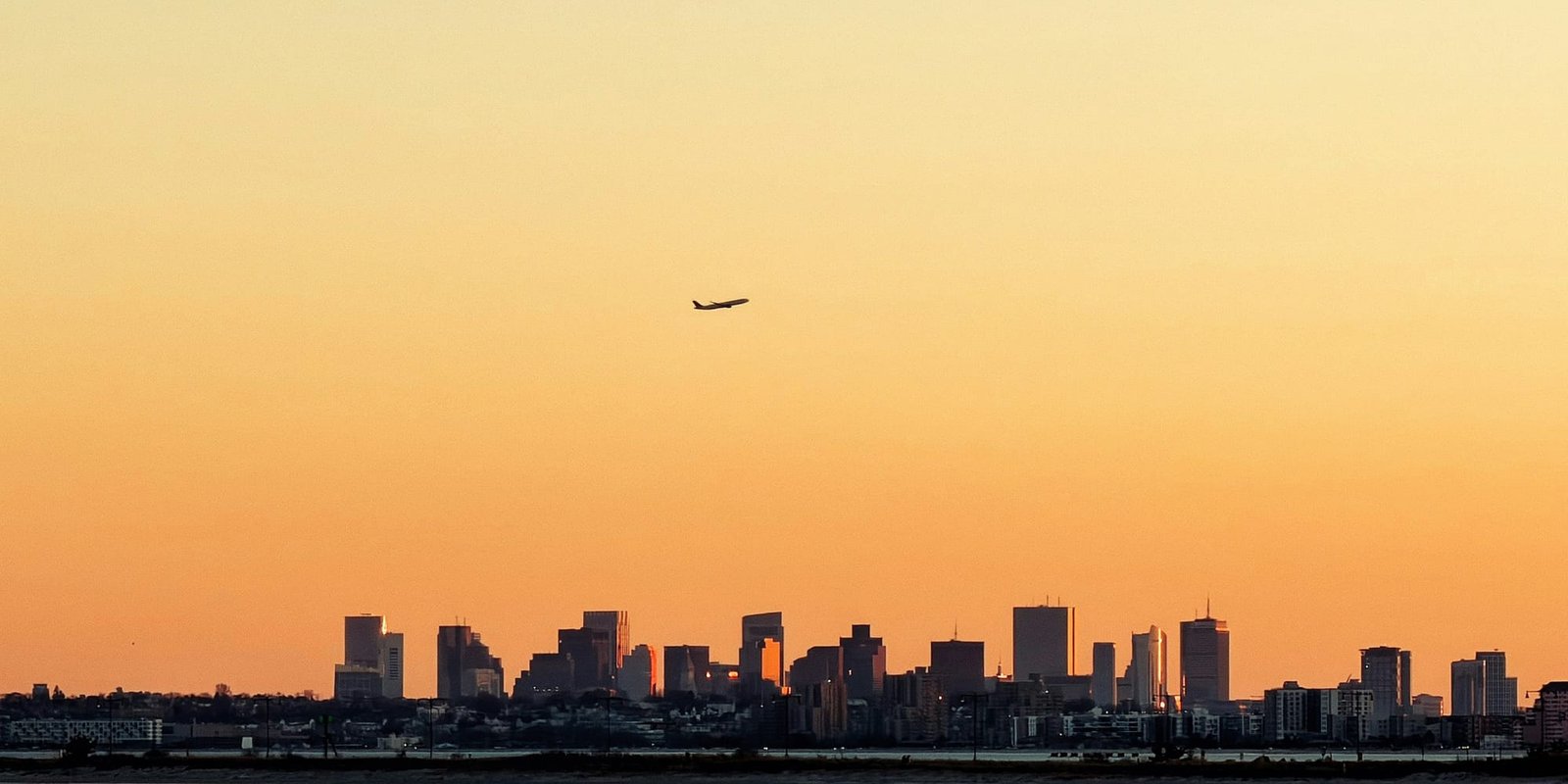 An airliner climbing above a city skyline at sunset